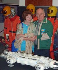 Catherine Schell and Nick Tate in front of 4 original spacesuits, and the original Eagle 2